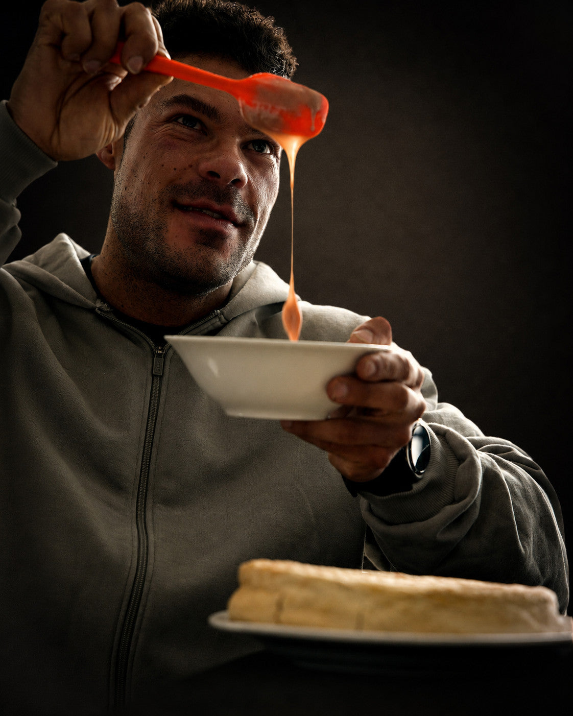 Wesley Vissers drizzling hot sauce over a bowl held to camera, plated food in the foreground